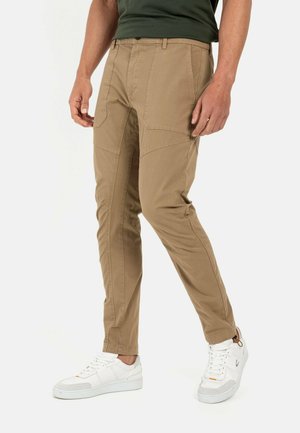 Beige cargo bukser med tætsiddende design, flere lommer og synlige syninger. Parret med hvide sneakers.