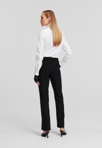 Witte langslavende shirt met knoopmanchetten, gecombineerd met zwarte op maat gemaakte broek met zijslits, afgemaakt met zwarte hakken.