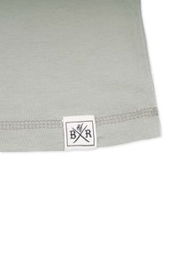 Lys grå t-shirt med en textured ribbet kant. Har et mærkepatch med sort skrift og krydsede pile.