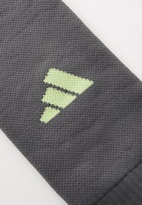 Grå strikket tekstil med et grønt geometrisk logo med tre nedover pekende trekanter, som indikerer merkeidentitet og design detalj.