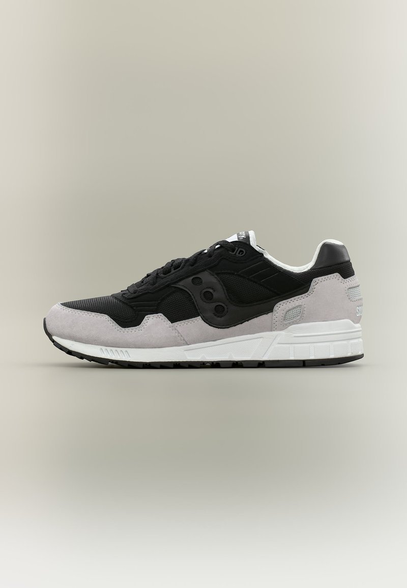 Μαύρο και γκρι αθλητικό παπούτσι με λευκή σόλα, λεπτομέρειες από δίχτυ και σουέντ, και πλευρικό πάνελ με λογότυπο σε ουδέτερο φόντο.