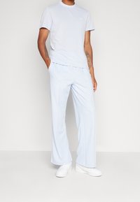 Jasnoniebieska koszulka z krótkim rękawem z logo na kołnierzyku, zestawiona z pasującymi jasnoniebieskimi spodniami o szerokich nogawkach i białymi trampkami.