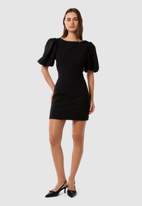 Abito nero con maniche a sbuffo, design aderente e taglio a ginocchio. Tessuto dalla consistenza liscia, scollo rotondo e dettagli di cucitura minimali.