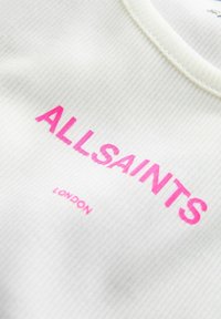 Biały prążkowany materiał z jasnoróżowym napisem "ALLSAINTS" oraz mniejszym napisem "LONDON" poniżej, na elemencie odzieży.