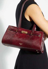 Burgundy leather handbag with a textured finish, dual top handles, gold-tone hardware, and a clasp detail at the front.