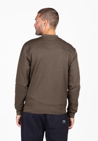 Sweat-shirt marron à manches longues avec un tissu texturé, col rond et poignets côtelés, présentant un détail de couture horizontale sur le haut du dos.