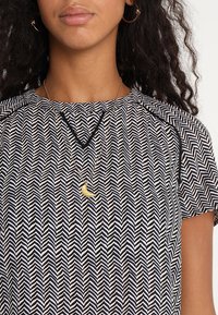 Blusa con patrón de chevrones en blanco y negro, de mangas cortas, que presenta un escote redondo y un delicado collar en forma de luna creciente dorada.