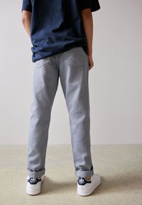 Vaqueros de mezclilla gris claro con corte recto, dobladillos enrollados y dos bolsillos traseros. Combinados con zapatillas blancas con un acento en azul marino.