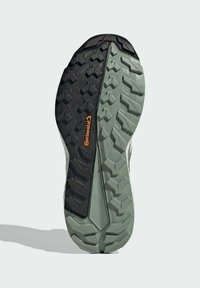 Musta ja vihreä kuminen kenkäpohja, jossa on teksturoitu kuvio, jossa on näkyvä oranssi logo ja monisuuntainen pito.
