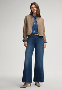 Giacca cropped a scacchi marrone, camicia di jeans blu, jeans a gamba larga blu e tacchi beige. Le caratteristiche includono chiusure con bottoni e polsini a contrasto.