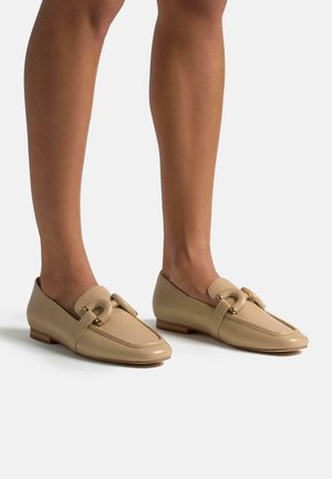 Beige Leder Slipper mit runder Zehenpartie, dekorativem Schnallendetail und niedrigem braunen Holzabsatz. Glatte Textur, minimalistisches Design.
