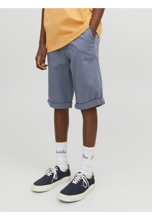 Szare szorty z podwiniętymi mankietami wykonane z materiału bawełnianego, z kieszeniami po bokach; zestawione z granatowymi butami i białymi skarpetkami z nadrukiem.