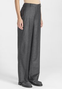 Szare wełniane spodnie o szerokich nogawkach i wysokim stanie, z przednimi kieszeniami i gładką fakturą, w połączeniu z ciemnoszarymi butami.