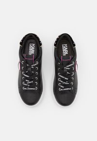 Černé syntetické tenisky s bílou podrážkou, zdobené dekorativními šňůrkami a logy. Zakulacená špička, polstrovaný límec a barevné akcenty na očkách.