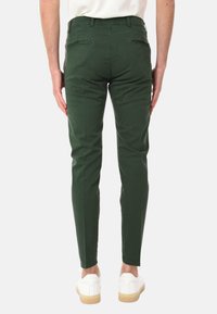 Pantaloni di cotone verdi a taglio slim, con due tasche posteriori e una texture liscia, abbinati a sneakers bianche e una camicia chiara.