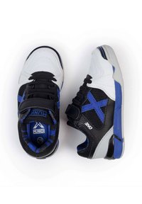 Zapatillas deportivas en blanco y negro con acentos en azul, que cuentan con una parte superior texturizada, cierres de cordones y una correa de velcro para mayor soporte.