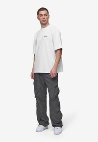 White oversized cotton t-shirt with a small graphic on the chest, paired with gray cargo pants featuring multiple pockets and zippers, white sneakers.