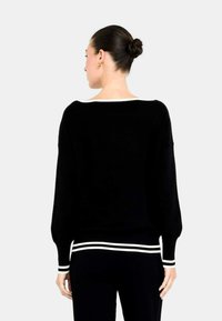 Maglione nero con una vestibilità ampia, scollo largo e maniche lunghe. Presenta dettagli a righe bianche sui polsini e sull'orlo. Tessuto liscio.