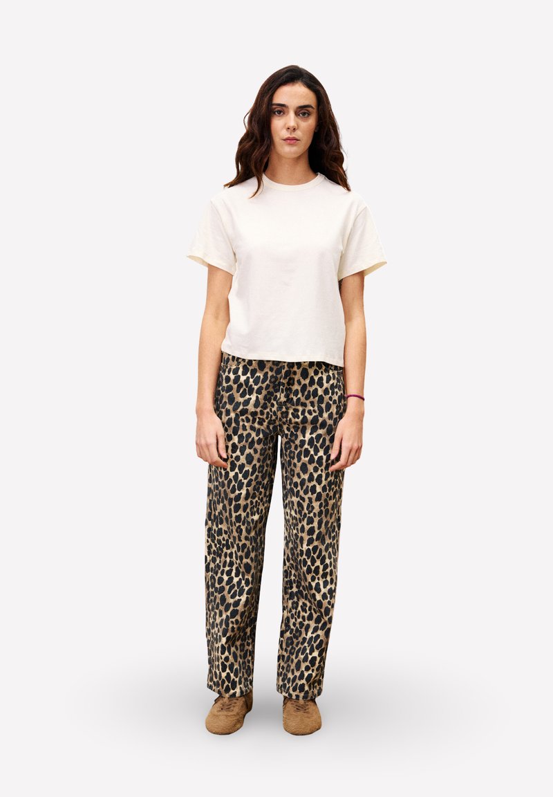 T-shirt crème à manches courtes associé à un pantalon large imprimé léopard noir et beige, présentant une coupe décontractée et un tissu doux. Chaussures brunes à enfiler.