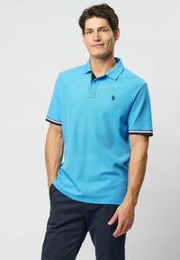 Lyseblå polo-shirt lavet af åndbart stof, med klassisk krave, tre-knaps placket og ærmer med kontraststriber.