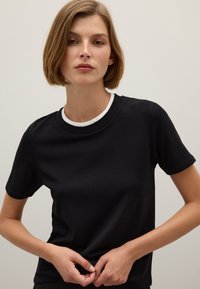 T-shirt in cotone nero con maniche corte e collo a girocollo, caratterizzato da un collo interno bianco. Texture liscia, design aderente. Nessun motivo o accento visibile.