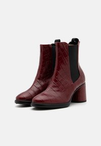 Botine vișinii cu un model lucios de crocodil, panouri laterale elastice și un toc masiv pentru un plus de înălțime și stabilitate.