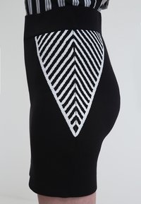 Gonna a tubino nera in maglia con un motivo geometrico a zigzag bianco sul retro. La texture è liscia e aderente.