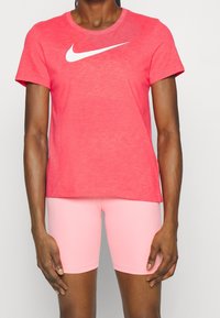 Camiseta roja de manga corta de Nike con un logo blanco Swoosh en la parte delantera, combinada con pantalones cortos de bicicleta rosas, con una textura suave y lisa.