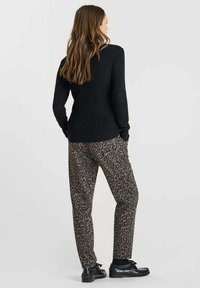 Pull ras du cou noir à côtes, pantalon en imprimé léopard dans des tons beiges et marron foncé, chaussures en cuir, texture lisse, coupe décontractée, vue de dos.
