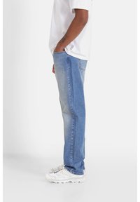 Jeans di denim azzurro chiaro con taglio dritto, caratterizzati da una finitura strappata e design a cinque tasche. Abbinati a scarpe da ginnastica bianche.