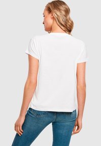 T-shirt bianco a maniche corte, in cotone, vestibilità comoda, colletto rotondo, design semplice, abbinato a jeans blu in denim.
