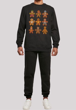 Schwarzer Sweatshirt mit neun Lebkuchen, die als Marvel-Superhelden dekoriert sind, getragen mit passenden schwarzen Hosen und weißen Turnschuhen.