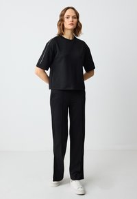 Czarny komplet odzieży sportowej składający się z krótkiego topu z okrągłym dekoltem i krótkim rękawem oraz pasujących spodni o wysokim stanie z bocznymi lampasami.