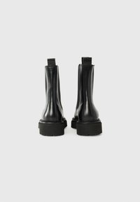 Bottines en cuir noir avec une finition lisse, bout arrondi, panneaux latéraux élastiques, et semelles en caoutchouc épaisses pour une meilleure traction.