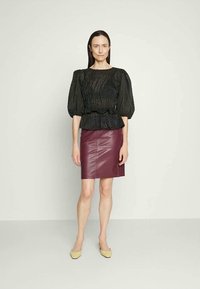Black textured blouse with balloon sleeves, peplum waist; paired with a burgundy leather skirt. Model wears yellow flats.