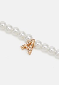 Perlesnor med et guld "A" charm, prydet med klare rhinestones, som har en glat, blank overflade og en ensartet, rund form.