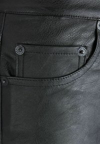 Zwarte leren broek met een voorzak met decoratieve metalen drukkers en zichtbare stiksels, vertonend een gladde en gestructureerde oppervlakte.