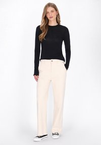 Zwarte longsleeve top, beigekleurige wijde broek, witte sneakers. Glad stof en een comfortabele pasvorm met een klassieke knoopsluiting op de broek.