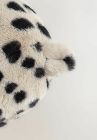 Rundes, samtiges Kissen, das mit cremefarbenem Kunstfell und schwarzen Punkten bezogen ist. Verfügt an einem Rand über ein kleines, weiches Schwanzdetail. Glatte Textur.