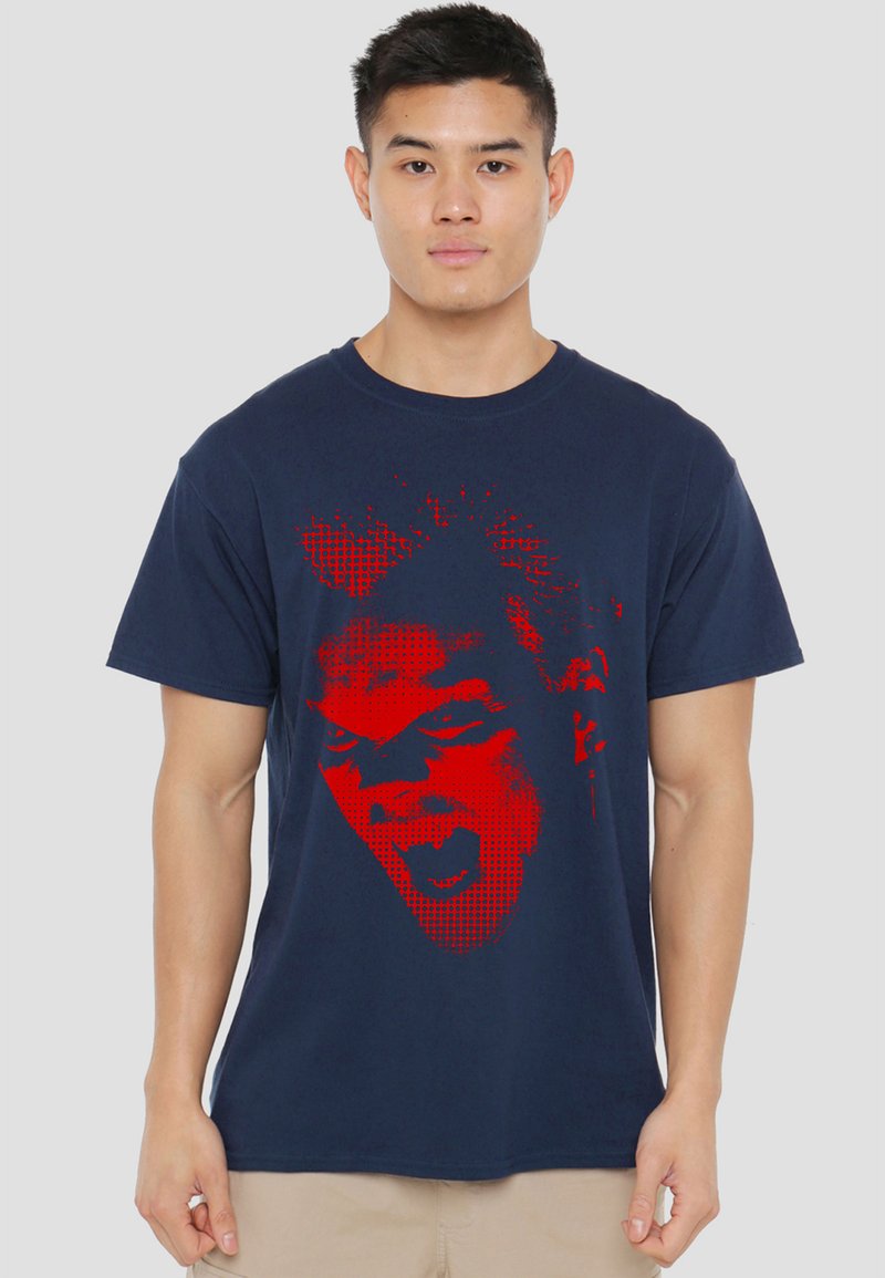 Young man wearing navy blue t-shirt with large red graphic of a screaming face on the front, standing against a plain background.