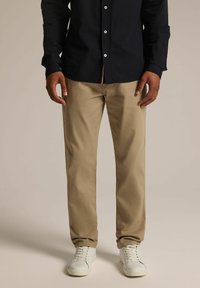 Beżowe bawełniane chinosy o prostym kroju, w zestawieniu z ciemnogranatową koszulą zapinaną na guziki. Białe sneakersy dopełniają outfit.