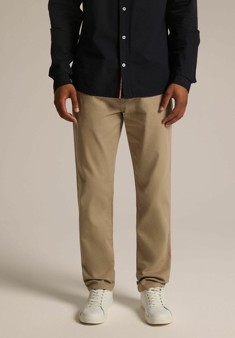 Beżowe bawełniane chinosy o prostym kroju, w zestawieniu z ciemnogranatową koszulą zapinaną na guziki. Białe sneakersy dopełniają outfit.