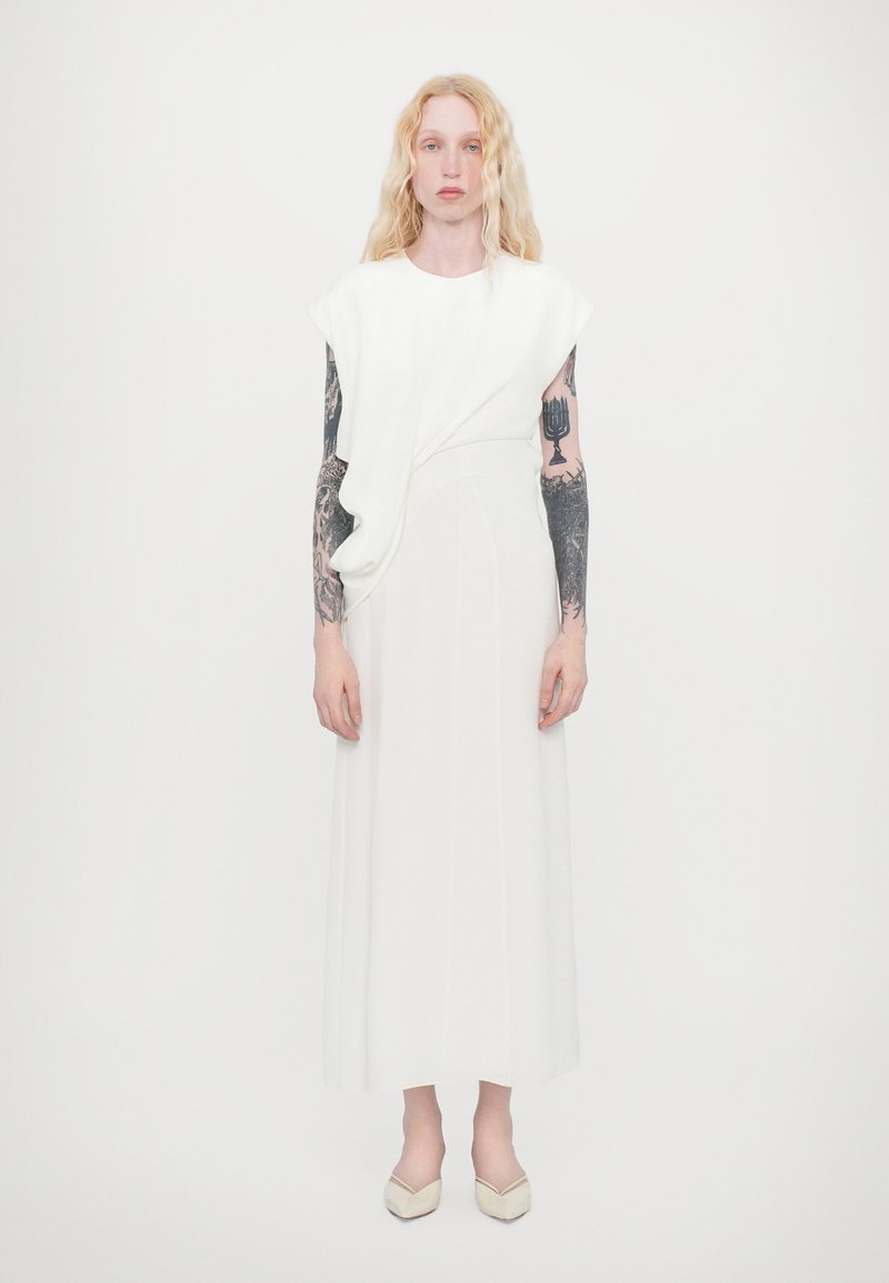Weißes Kleid mit asymmetrischem Drapieren an der Schulter, lange, fließende Silhouette, gefertigt aus glattem Stoff, kombiniert mit beigefarbenen Ballerinas.