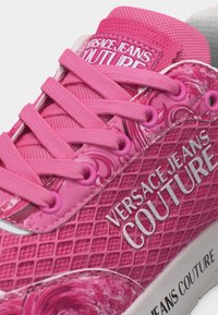 Φωτεινό ροζ sneaker της Versace Jeans Couture με υφασμάτινο σχέδιο, ροζ κορδόνια και λευκό κείμενο λογότυπου στο πλάι και στη γλώσσα.