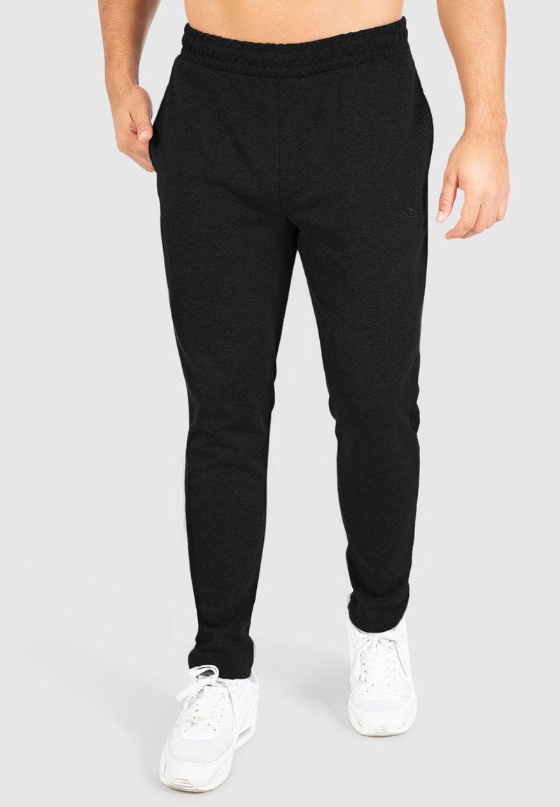 Schwarze, taillierte Jogginghose aus weichem Stoff, mit einem elastischen Bund und seitlichen Taschen. Kombiniert mit weißen Sneakern.