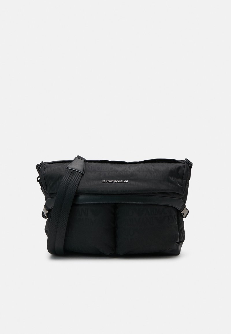 Czarna torba listonoszka z nylonu o wyściełanym designie, regulowanym paskiem i tłoczonym logo. Posiada zamknięcie na zamek błyskawiczny oraz gładką teksturę.