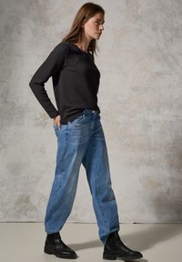 Svart långärmad topp med ett strukturerat zigzag-mönster, i kombination med ljusblå löst sittande jeans och svarta ankelskor.