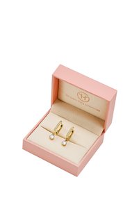 Guld hoops øreringe med en lille klar ædelsten vedhæng, præsenteret i en blød pink æske med en beige fløjlsindvendig og logo.