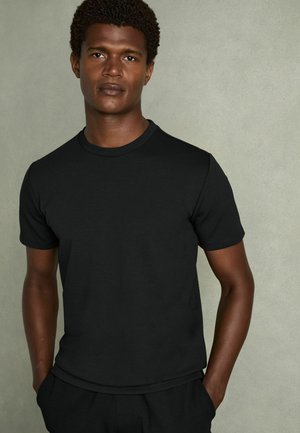 Tricou negru cu mânecă scurtă, fabricat din bumbac moale, având un guler rotund și un design ajustat. Textură fină și stil minimalist.