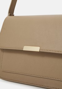 Borsa in finta pelle beige con una texture liscia, caratterizzata da una chiusura in tono oro, linee pulite e un design strutturato.